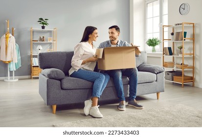 Excited young couple looking at each other while unpacking cardboard box at home. Man and woman customers unboxing parcel receiving online shop order or gift. Delivery and postal service concept - Powered by Shutterstock