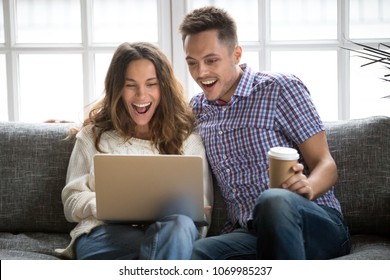 Excited young couple looking at laptop screen sitting at home on sofa, surprised cheerful man and woman happy with good news online, amazed by special email offer sale, delighted by new opportunity