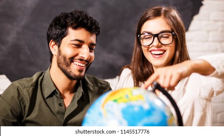 Excited Young Couple Planning Their Holiday Holding Up A Globe And Pointing To A Travel Destination