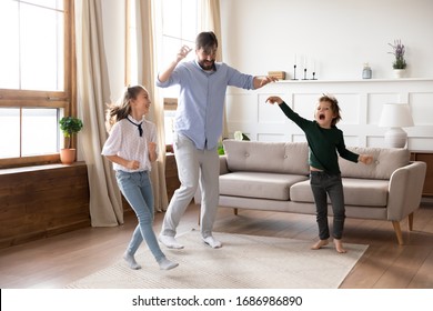 Excited Young Father Enjoying Funny Family Activity With Small Kids In Living Room. Energetic Little Children Siblings Dancing To Favorite Pop Music With Cheerful Daddy At Free Weekend Time At Home.