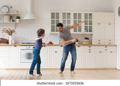 Excited young father and little son feel overjoyed dancing together in spacious modern kitchen, happy dad and small preschooler have fun at home engaged in funny activity, enjoy leisure weekend
