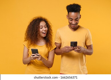 Excited Young Friends Couple African American Guy Girl In Casual Clothes Isolated On Yellow Orange Background. People Lifestyle Concept. Mock Up Copy Space. Using Mobile Phone, Typing Sms Message