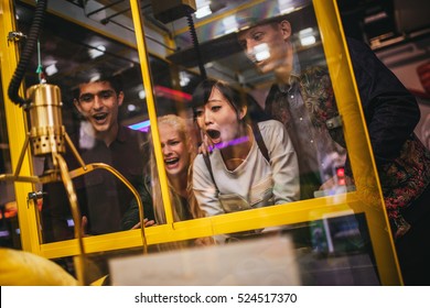 Excited young friends playing toy grabbing game at amusement park. Happy woman selecting a random soft toy in a vending machine.