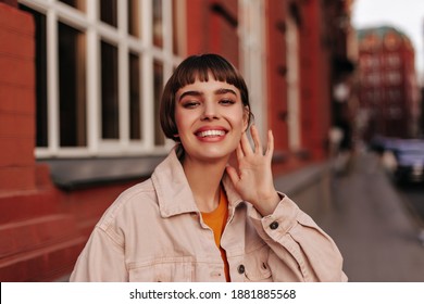 Excited young girl in pink denim jacket smiles sincerely outdoors. Happy pretty short-haired woman walks outside. - Powered by Shutterstock