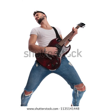 excited young guitarist playing the guitar  and leaning back while standing on white background