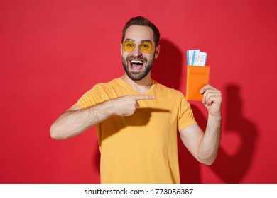 Excited young guy in yellow t-shirt glasses isolated on red background. Passenger traveling abroad to travel on weekends getaway. Air flight journey concept. Point index finger on passport tickets - Shutterstock ID 1773056387