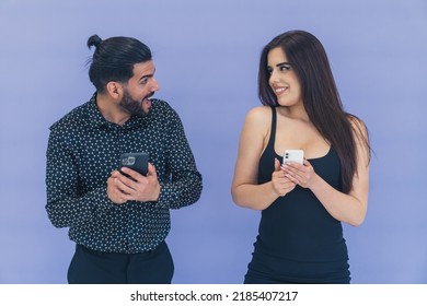 Excited Young Happy Couple Standing Next To Each Other Texting On Smartphones Looking At Each Other. Studio Shot. High Quality Photo