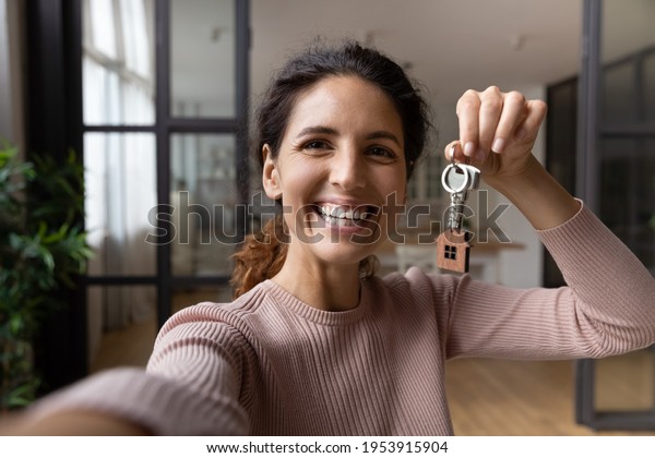 Excited young hispanic lady tenant buyer wish to\
keep in memory moving to new home take selfie on phone with keys in\
hand. Happy woman proud of buying flat make video call to friend\
show key to camera