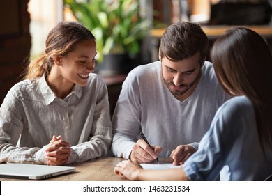 Excited Young Husband And Wife Sign Contract Taking Loan Or Mortgage From Female Banking Specialist, Overjoyed Millennial Couple Feel Happy Closing Deal Put Signature On Agreement Meeting With Realtor