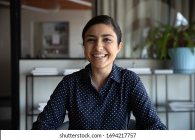 Excited young indian ethnicity woman looking at camera, holding funny conversation with colleagues online, webcam view. Head shot millennial hindu female worker laughing, having fun in office.