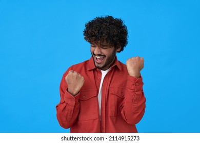 Excited young indian man winner showing yes gesture feeling happy about sport betting lottery win, winning game, celebrating success or new opportunity isolated on blue background.