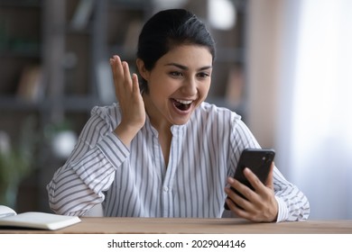 Excited Young Indian Woman Look At Cellphone Screen Shocked By Unexpected Online Sale Offer Or Promotion Deal. Overjoyed Stunned Ethnic Female Use Smartphone Get Amazing News Message On Gadget.