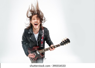 Excited Young Man In Black Leather Jacket With Electric Guitar Shouting And Shaking Head Over White Background