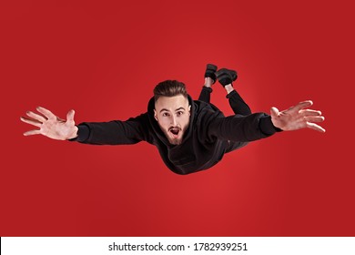 Excited young man is flying through the air in a state of gravity.  Studio portrait on a red background.