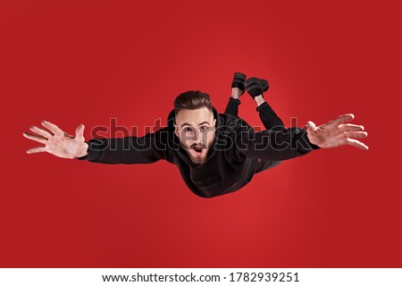 Excited young man is flying through the air in a state of gravity.  Studio portrait on a red background.