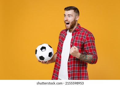Excited young man football fan in basic shirt cheer up support favorite team with soccer ball clenching fist doing winner gesture isolated on yellow background studio. People sport leisure concept