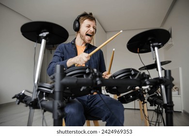 Excited young man with headphones hitting electric drum set during repetition at home. Online music lessons. - Powered by Shutterstock