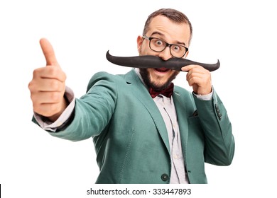 Excited Young Man Holding Fake Moustache On His Face And Giving A Thumb Up Isolated On White Background