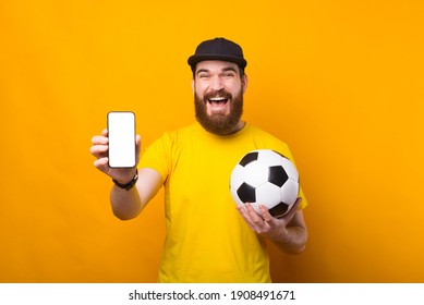 An excited young man is holding a soccer ball and a phone smiling . - Powered by Shutterstock