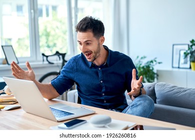 Excited young man shouting at laptop while working at home