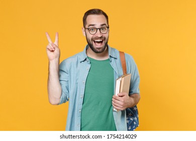 Excited young man student in casual clothes glasses with backpack hold books isolated on yellow background studio portrait. Education in high school university college concept. Showing victory sign