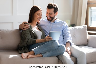 Excited young married couple resting on sofa, watching comedian funny movie on computer tablet, enjoying free weekend leisure time together. Happy family spouses cuddling, shopping online at home. - Powered by Shutterstock