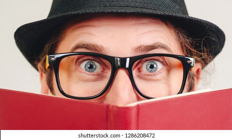 Excited Young Nerd Guy Holding Book. Nerd In Glasses. Funny Man Looking To Camera. Never Too Late To Study. Amazing Man Has Great Idea. Male Nerd Hiding Behind Books. Nerd Hipster Guy In Hat