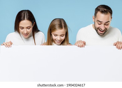 Excited young parents mom dad with child kid daughter teen girl in sweaters hold big white empty blank billboard mock up copy space isolated on blue background studio. Family day parenthood concept