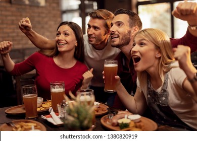 Excited Young People Watching Sports Match On TV While Drinking Beer And Eating In A Pub. 