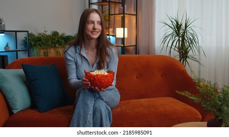 Excited Young Pretty Woman Sitting On Sofa Eating Popcorn And Watching Interesting Tv Serial, Sport Game, Film, Online Social Media Movie Content Online At Home. Girl Enjoying Domestic Entertainment