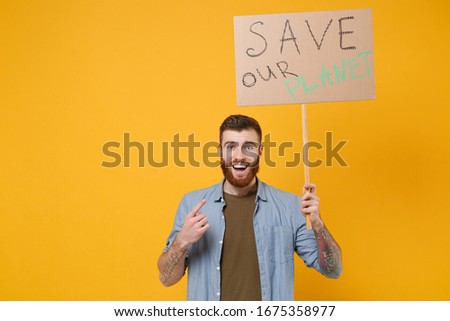 Excited young protesting man guy point index finger on protest sign broadsheet placard on stick isolated on yellow background. Stop nature garbage ecology environment protection concept. Save planet
