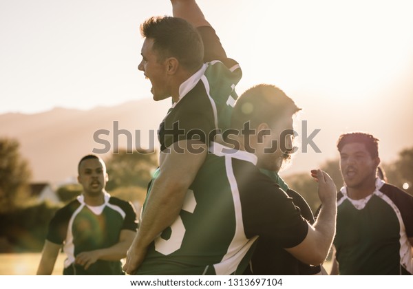 Excited young rugby\
players celebrating a win at the sports field. Rugby team enjoying\
after the victory.
