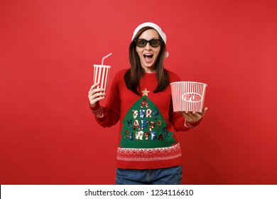 Excited young Santa girl in 3d imax glasses watching movie film holding popcorn, cup of soda isolated on red wall background. Happy New Year 2019 celebration holiday party concept. Mock up copy space