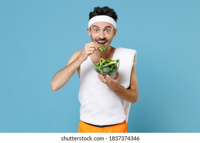 Excited Young Sporty Fitness Man With Thin Skinny Body Sportsman In Headband Shirt Shorts Hold Vegetable Salad In Glass Bowl Eating Isolated On Blue Background. Workout Gym Sport Motivation Concept