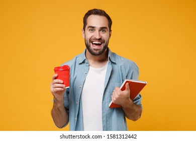 Excited young student man in casual blue shirt posing isolated on yellow orange wall background, studio portrait. People lifestyle concept. Mock up copy space. Holding notebook, cup of coffee or tea - Shutterstock ID 1581312442
