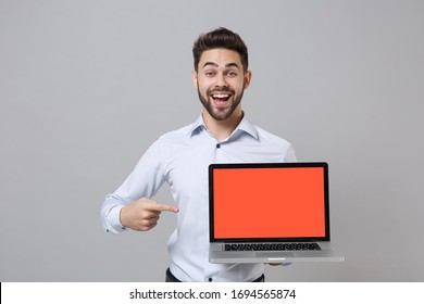Excited young unshaven business man in light shirt posing isolated on grey background. Achievement career wealth business concept. Pointing index finger on laptop pc computer with blank empty screen