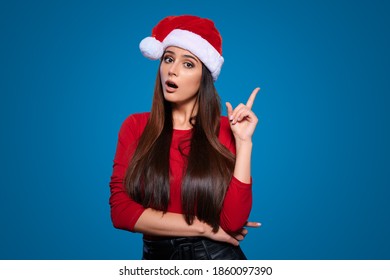 Excited young woman in Christmas Santa hat showing or pointing with finger away on blue isolated background