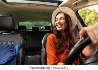 Excited young woman driving vehicle confidently, wearing hat and seatbelt, view from inside car interior at sunny day - Powered by Shutterstock