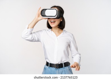 Excited young woman enter virtual reality in her glasses. Asian girl using vr headset, standing over white background - Powered by Shutterstock