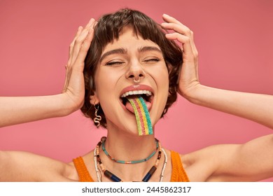 excited young woman in her 20s tasting sweet and sour candy strip on her tongue, pink background - Powered by Shutterstock