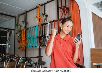 Excited Young Woman Looking On Mobile Phone Screen At Bike Shop