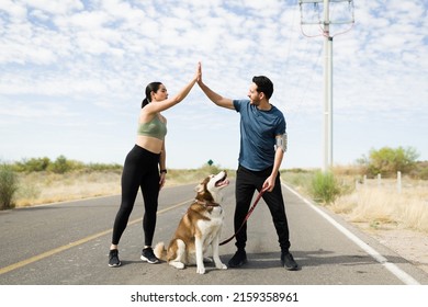 Excited Young Woman And Man Making A High Five And Celebrating Finishing A Running Race With Their Dog 