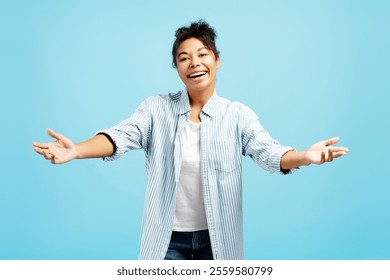 Excited young woman with open arms, offering a warm embrace and expressing happiness on a vibrant blue background - Powered by Shutterstock