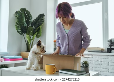 Excited Young Woman Opening Box While Her Cute Dog Sitting Near Her On The Table