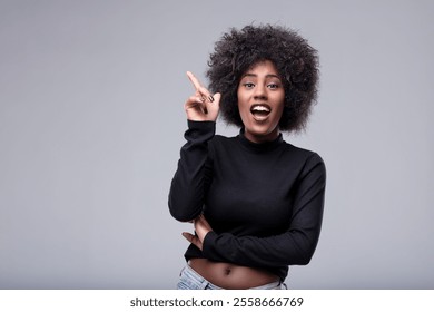 Excited young woman pointing her finger upward, showcasing a brilliant idea while gazing at the camera with an expression of surprise and joy, embodying creativity and inspiration - Powered by Shutterstock