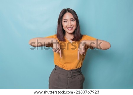 An excited young woman presenting and pointing downwards the copy space, isolated on blue background