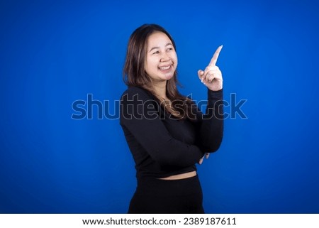 An excited young woman presents and points up the copy space, isolated on a blue background