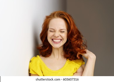 Excited Young Woman Pulling A Goofy Face With A Broad Smile As She Plays With Her Shoulder Length Red Hair