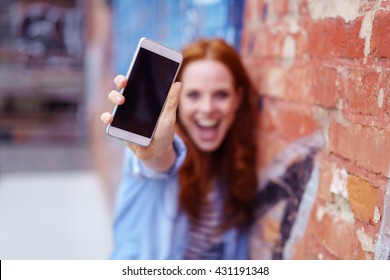 Excited Young Woman Screaming And Showing The Blank Screen Of Her Mobile Phone To The Camera, Focus To The Phone