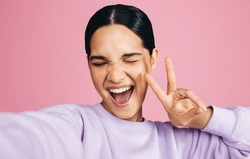 Excited Young Woman Taking A Selfie In A Studio, She Makes A Peace Sign With An Expression Of Joy On Her Face. Woman Having Fun Capturing Her Moments Of Self Confidence And Positivity.